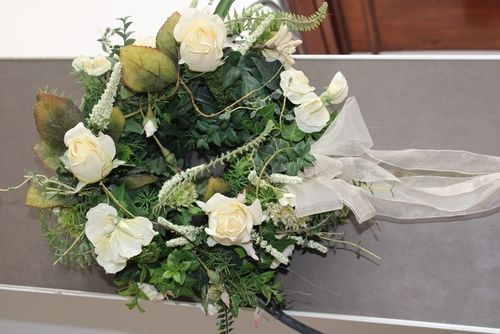 Dekorativer grüner Kranz mit weißen Rosen (Kunstblumen) und weißen Bändern